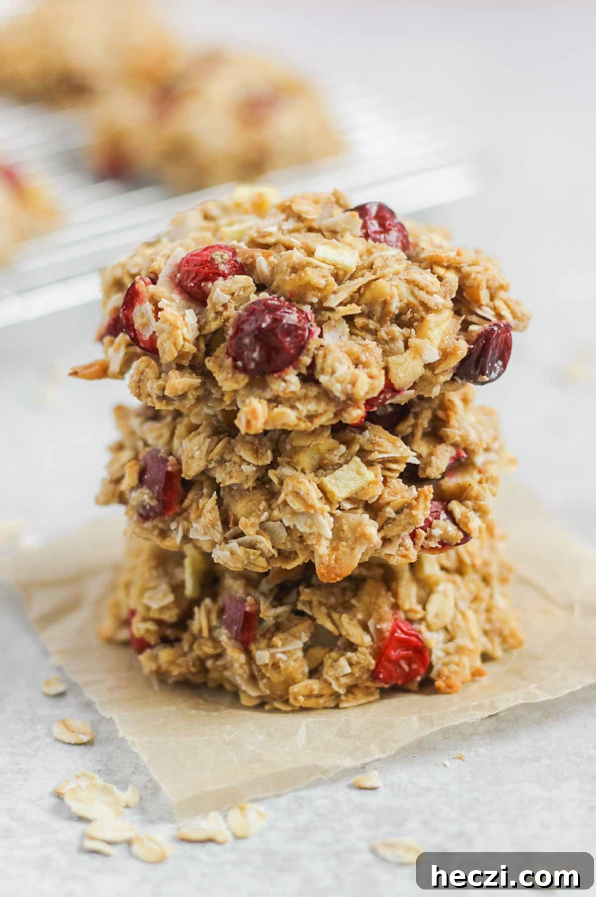 Three cranberry apple oatmeal breakfast cookies stacked on top of each other on a square piece of parchment paper.