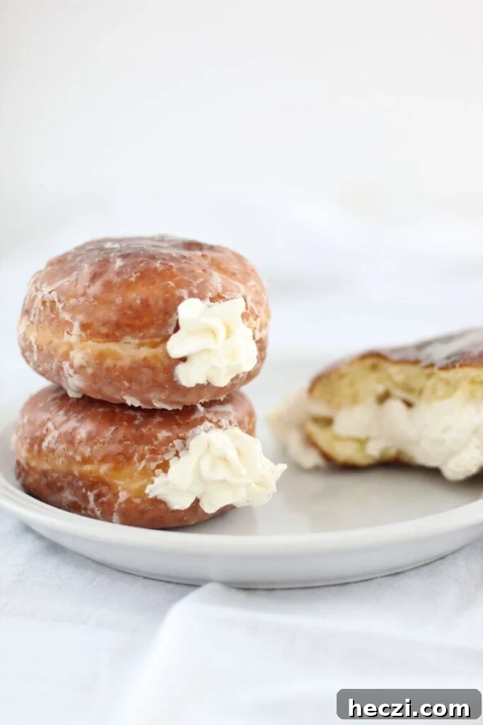 Light and Fluffy Gluten-Free Yeast Donuts Recipe 7 two stacked cream donuts on white plate with a half of one broken open to reveal cream filling.