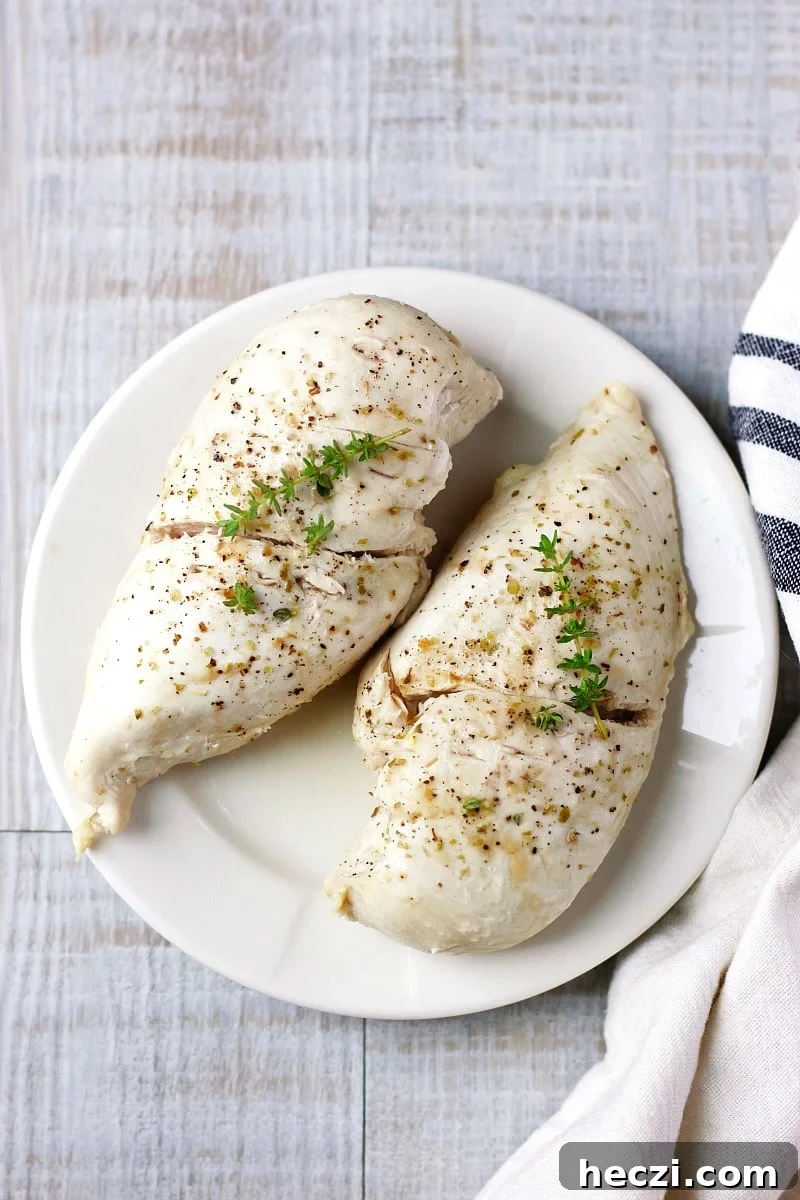 Steamed chicken breasts with herbs on a white plate and a white and black dish towel.
