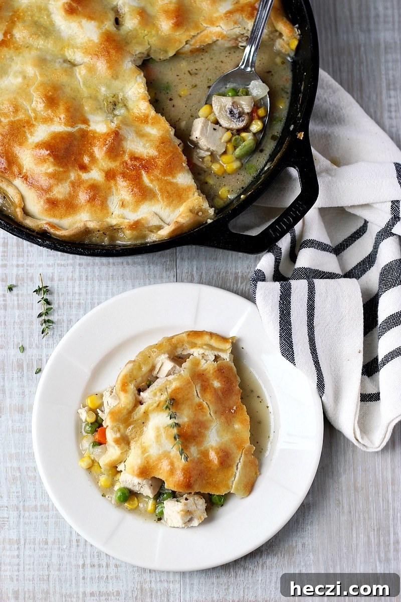 Skillet Chicken Pot Pie in a black cast iron skillet with a spoon and white and black dish towel and chicken pot pie on a white plate.