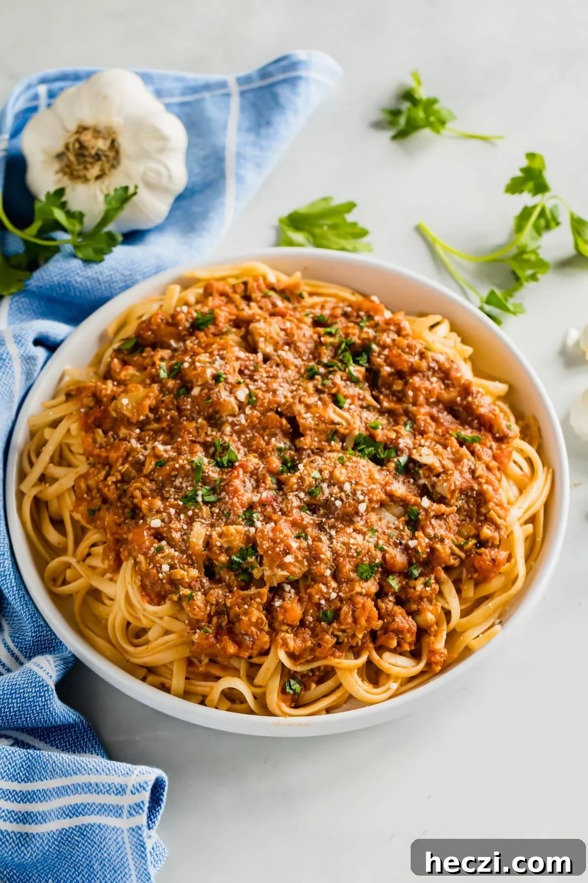 Red Clam Sauce Recipe for Pasta: Simple Italian-Style Sauce 2 A bowl of linguine and clams next to a blue towel with some garlic and parsley around it.