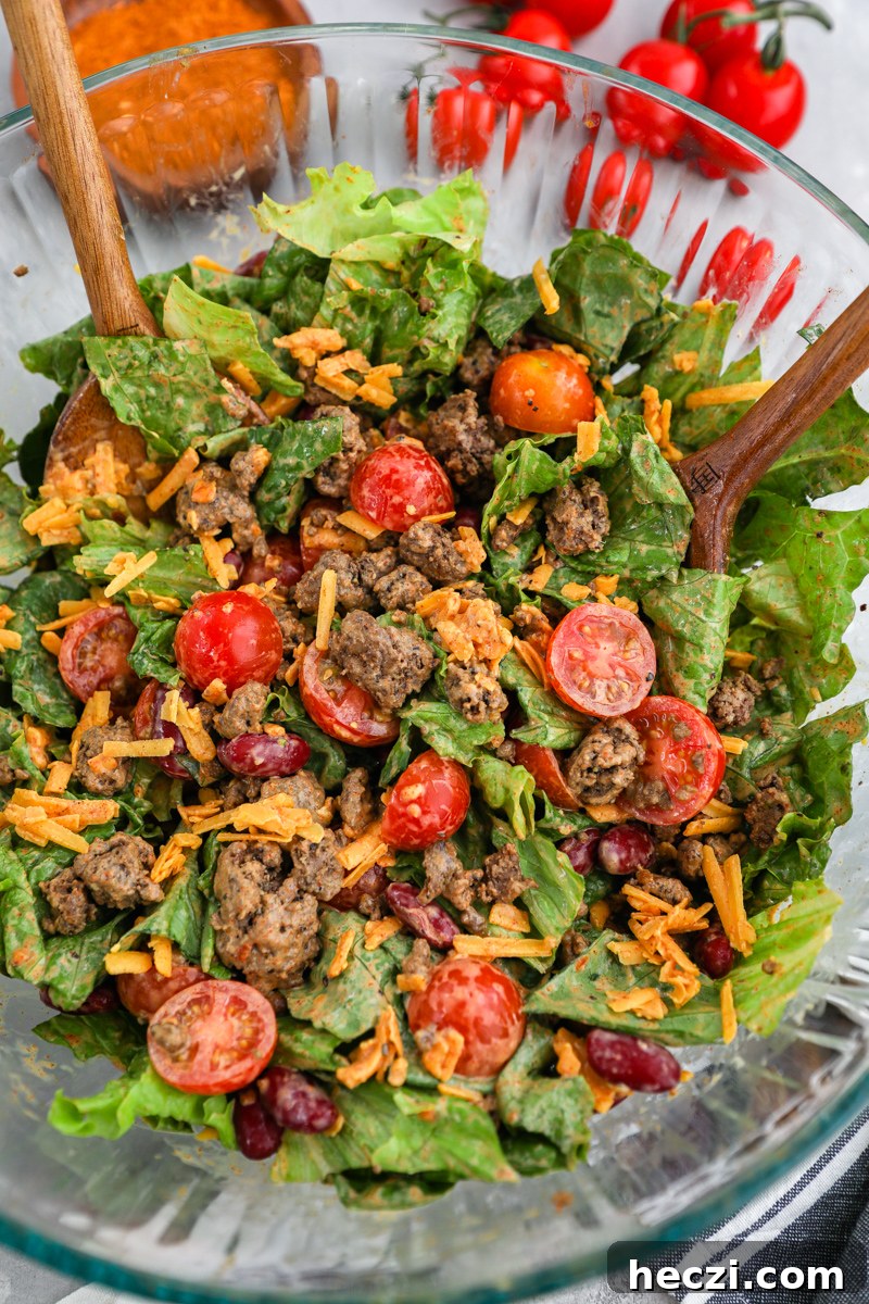A large clear mixing bowl filled with taco salad freshly tossed in dressing