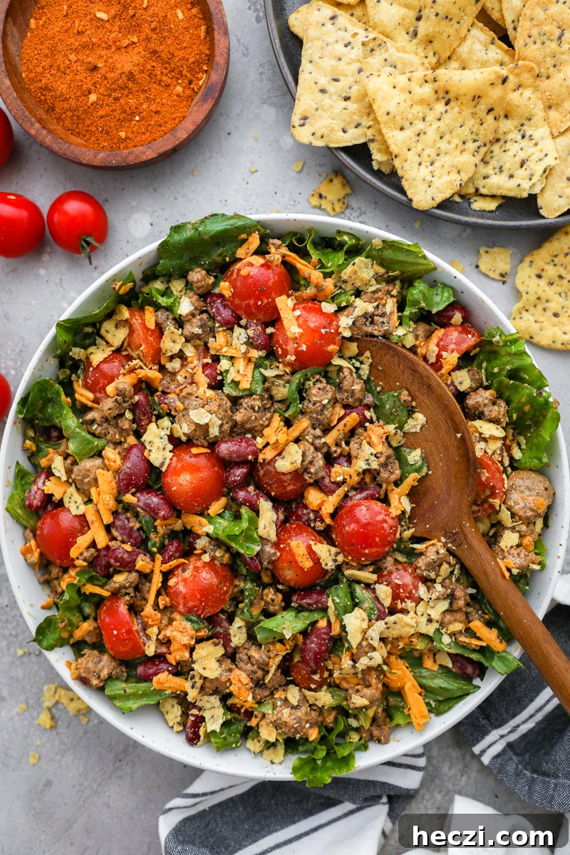 A large white serving bowl filled with easy taco salad salad surrounded by a plate of tortilla chips and a small bowl of taco seasoning