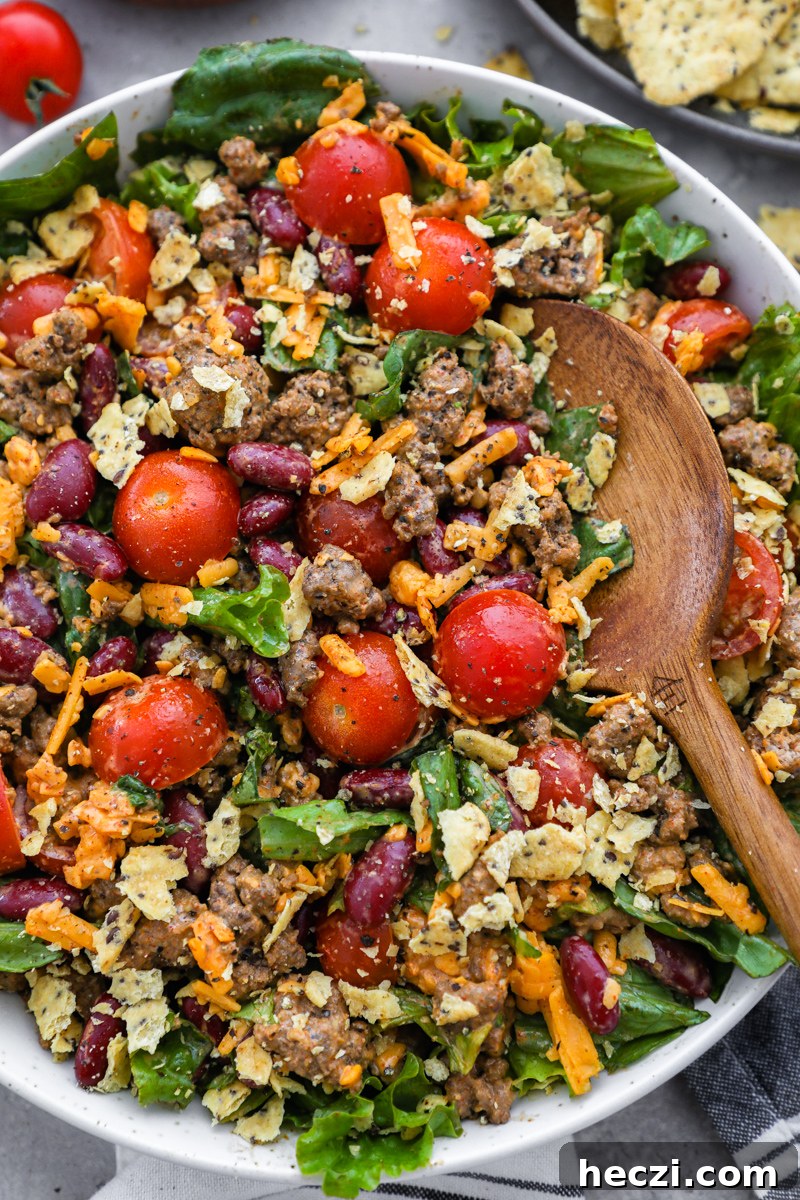 A close up photo of easy taco salad made with ground beef, kidney beans, tomatoes, cheddar cheese, tortilla chips and zesty taco dressing