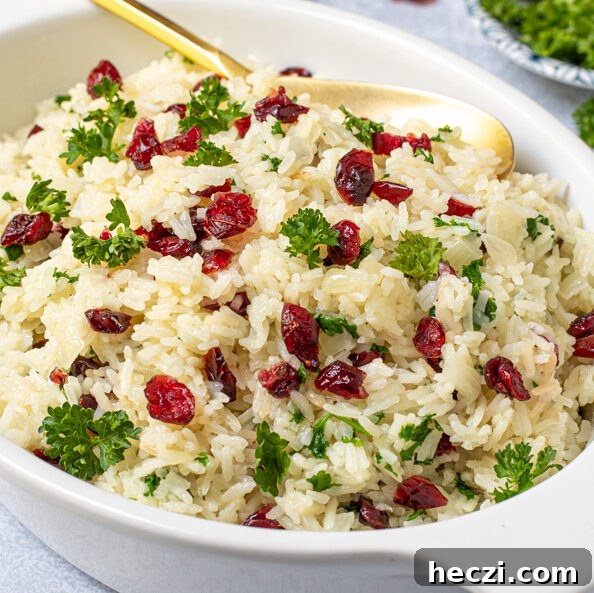 Sheet Pan Chicken Legs with Roasted Sweet Potatoes 11 A white serving dish with a gold spoon in white rice pilaf with dried cranberries and fresh parsley.