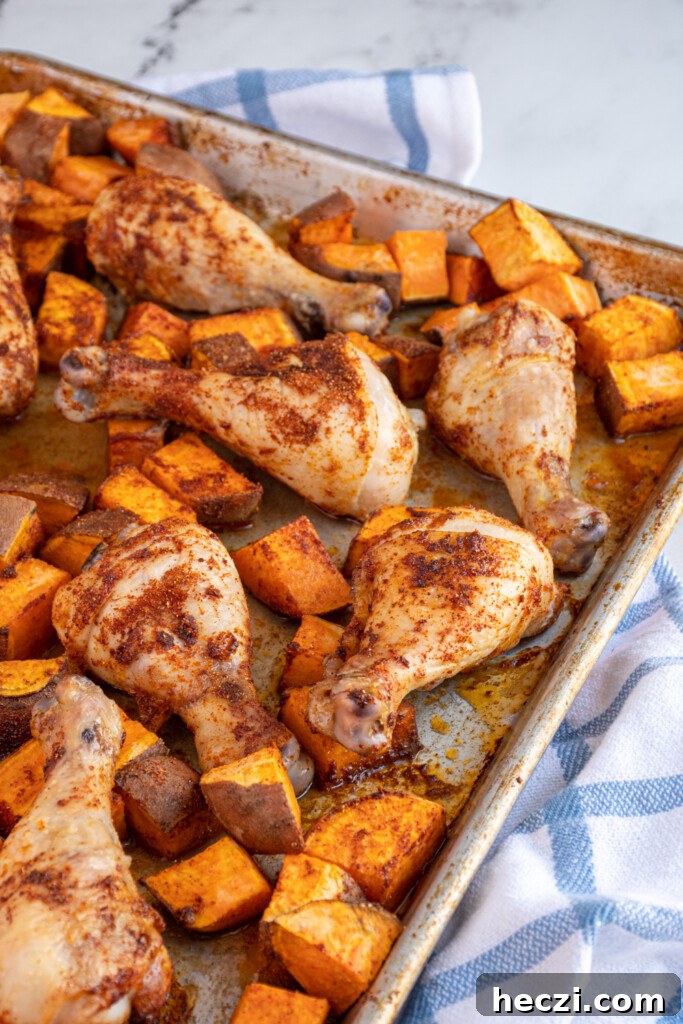 Sheet Pan Chicken Legs with Roasted Sweet Potatoes 8 Photo of part of a sheet pan that is full of baked chicken legs and sweet potato chunks.