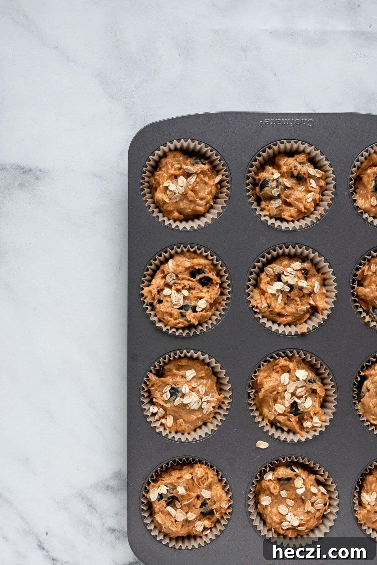 Blueberry Banana Oat Oatmeal Muffins for Breakfast 6 Banana blueberry oatmeal muffin batter divided evenly in a dark muffin tin before baking.