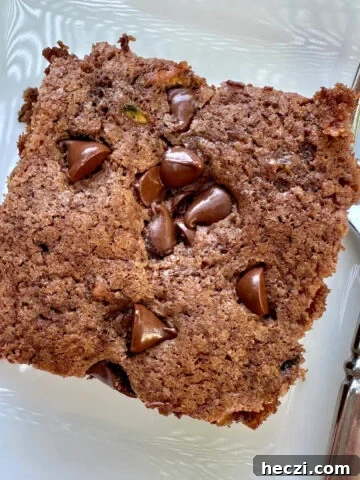A serving of moist chocolate zucchini cake on a plate with a fork.