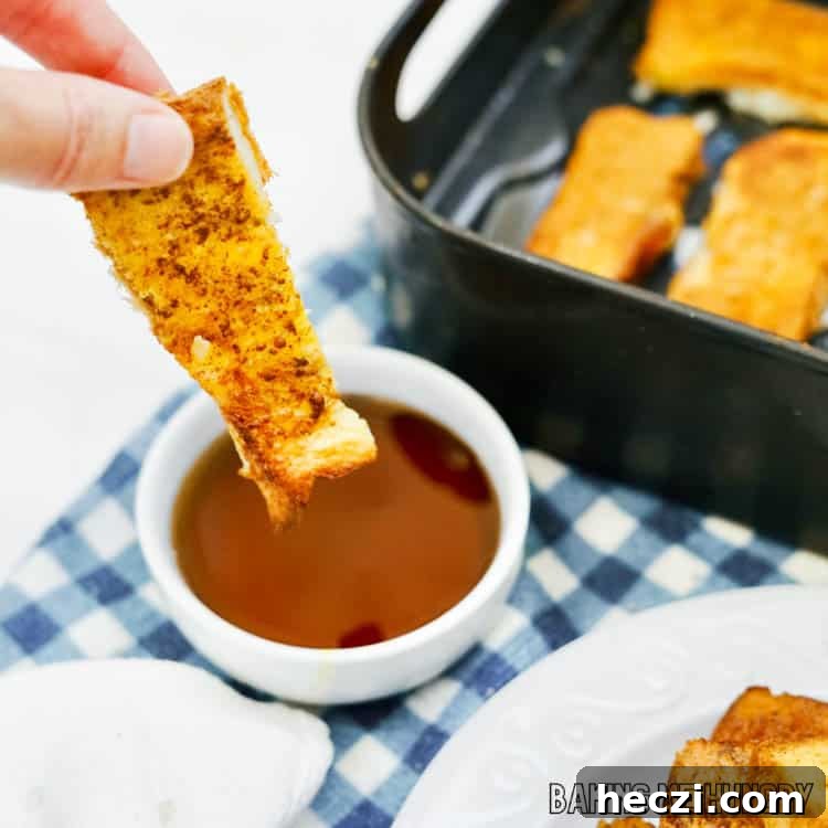 hand dipping french toast stick in syrup