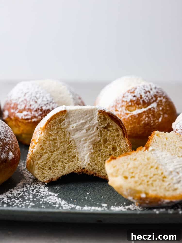 These airy, cream-filled pastries are called maritozzi and a must-make for any dessert lover. The buns have a soft, tender texture that pairs perfectly with the luscious vanilla filling! Top them off with a dusting of powdered sugar for a sweet Italian treat that everyone will love. Hero image of maritozzi buns. One is cut in half so the filling inside can be seen.