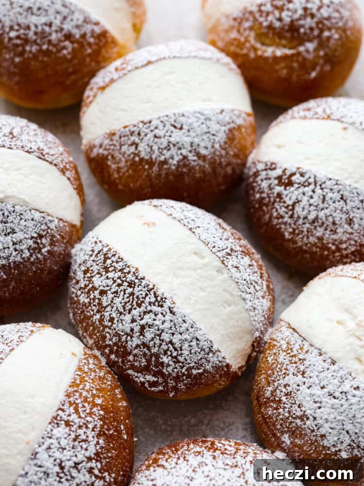 These airy, cream-filled pastries are called maritozzi and a must-make for any dessert lover. The buns have a soft, tender texture that pairs perfectly with the luscious vanilla filling! Top them off with a dusting of powdered sugar for a sweet Italian treat that everyone will love. Top-down view of maritozzi, cream-filled buns.