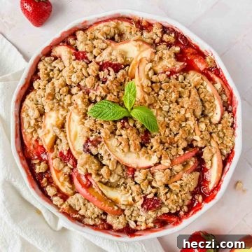 cooked strawberry apple crisp garnished with fresh mint and strawberries on pink tiled backdrop.