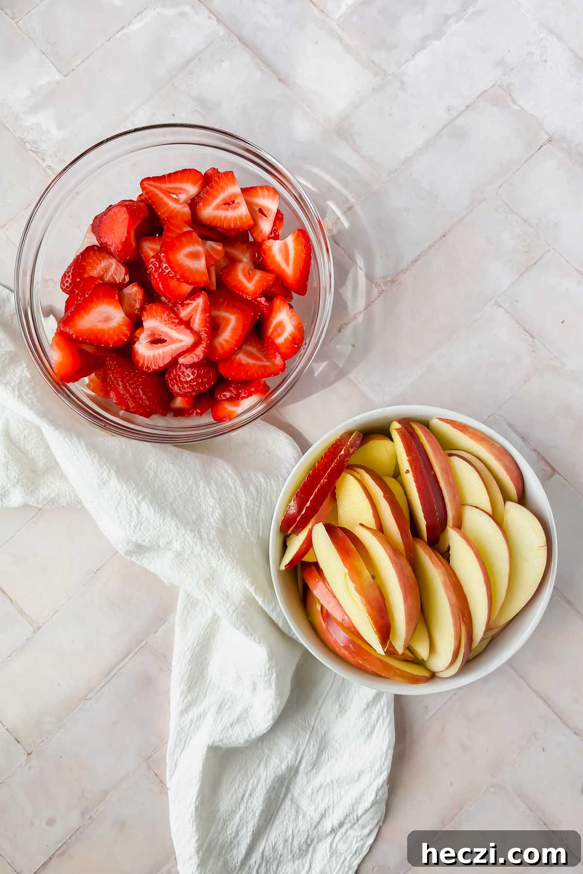 washed strawberries and apples sliced in individual bowls on pink background.