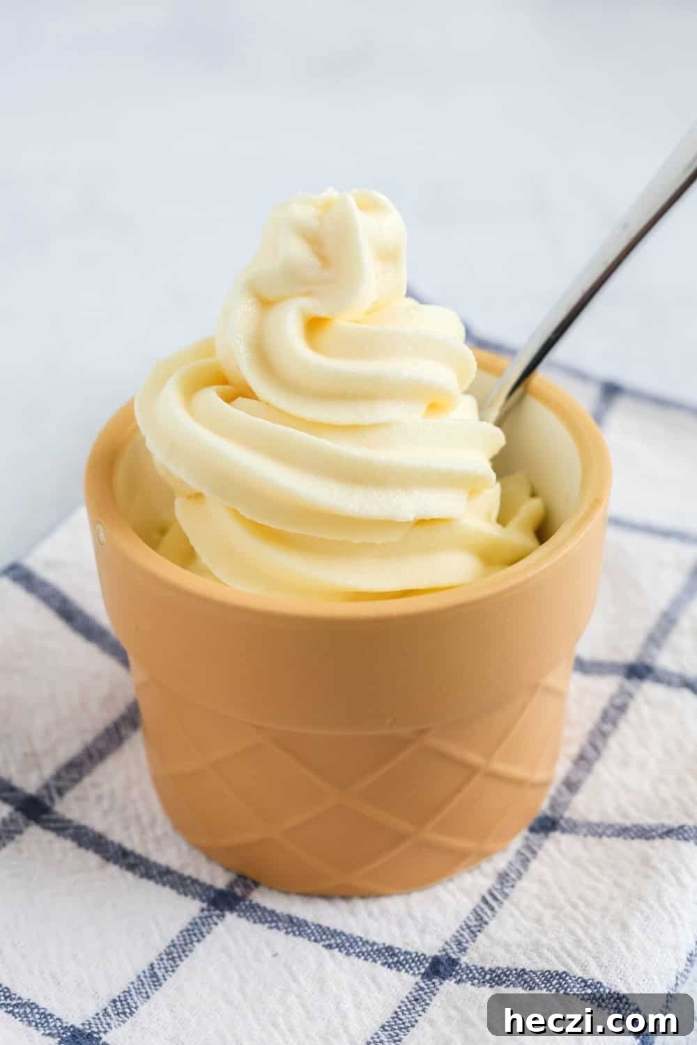 side view of a cup of Ninja Swirl by Creami vanilla soft serve with a spoon in it.