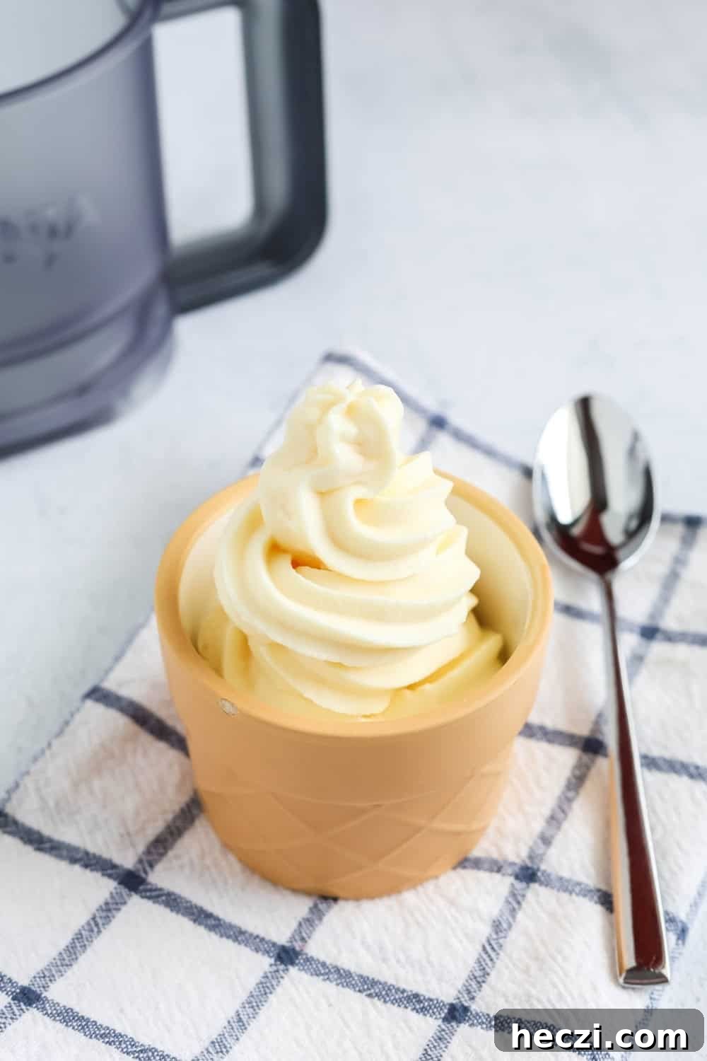 Homemade vanilla soft serve ice cream served in a dessert cup. A spoon and a Ninja Creami Swirl outer bowl are next to the cup.