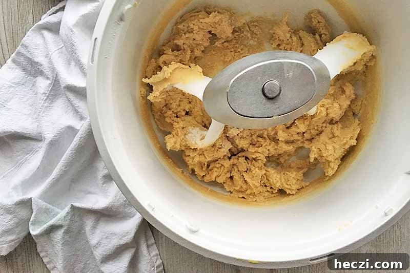 Horizontal image of a thick dough in a white mixing bowl.