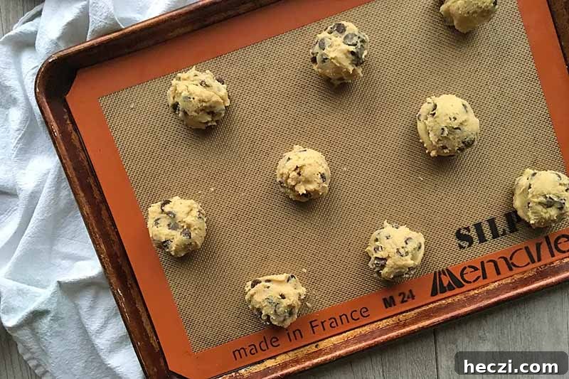Horizontal image of mounds of unbaked dough on a baking sheet lined with a silicone mat.