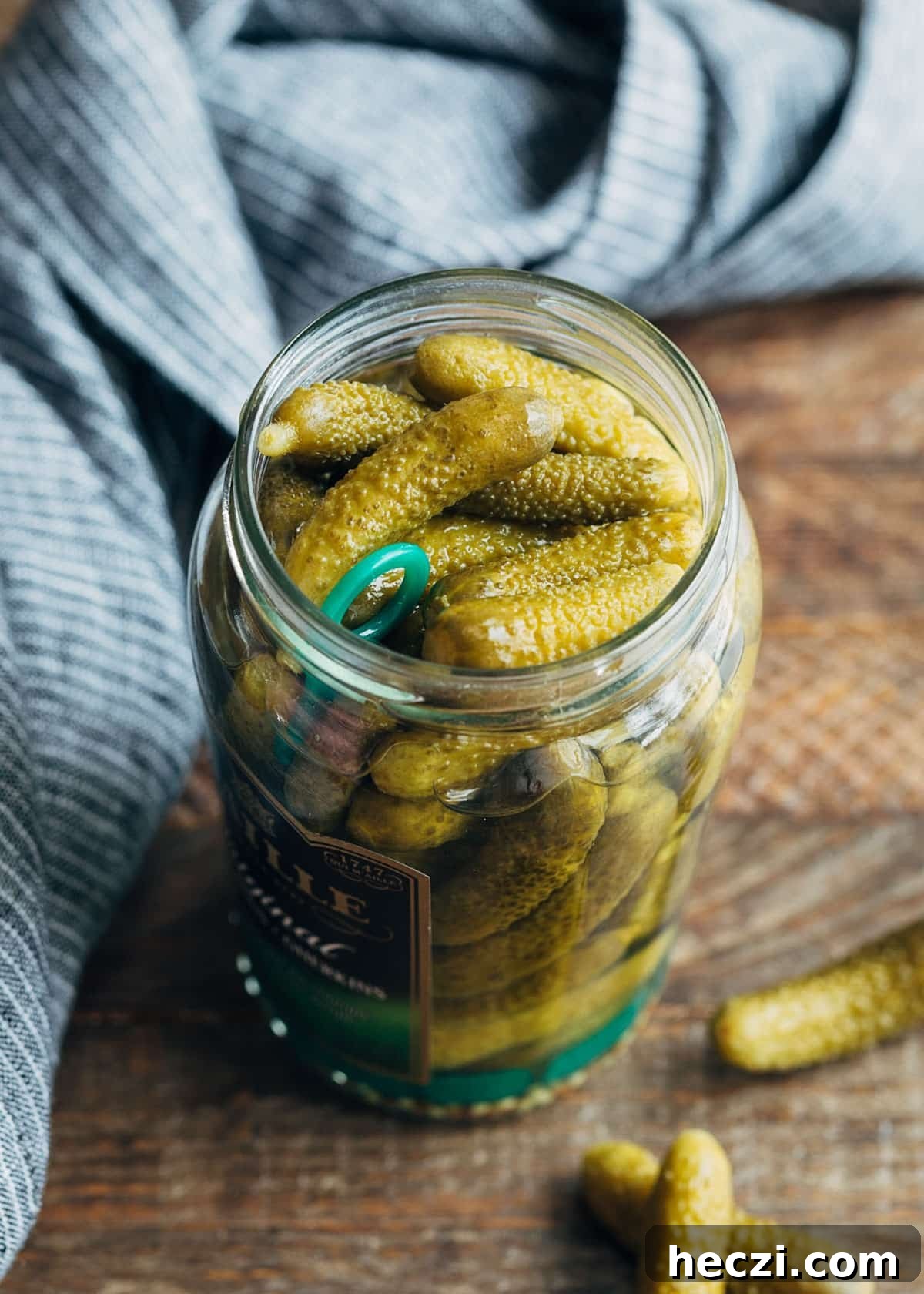 Cornichons: What They Are and 10 Ways to Use Them 2 cornichons in a glass jar on a wood board with a light blue napkin
