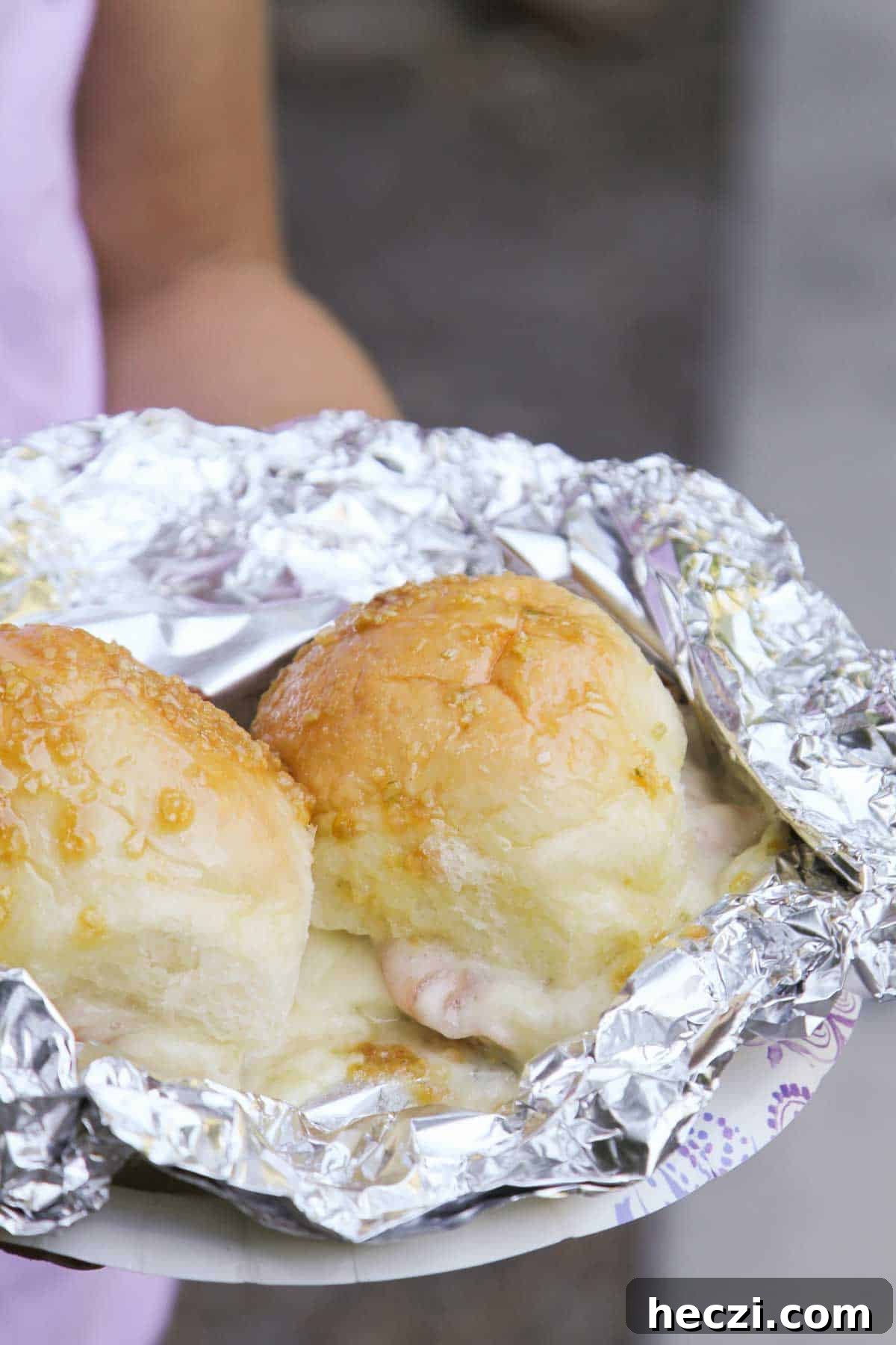 Two Hot Ham and Cheese Campfire Sandwiches in foil on a paper plate.