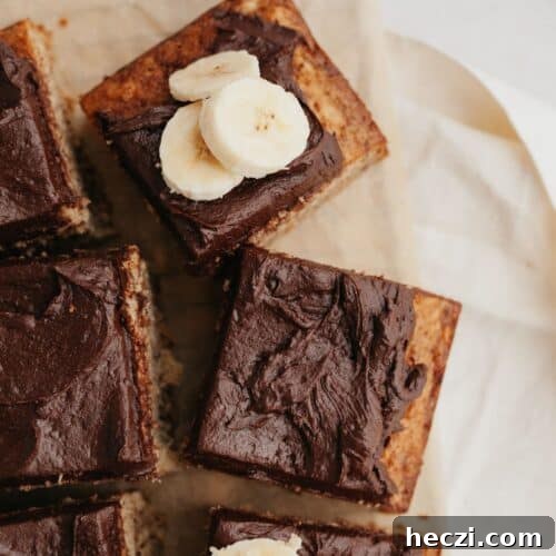 Squares of banana cake with chocolate frosting on parchment paper.
