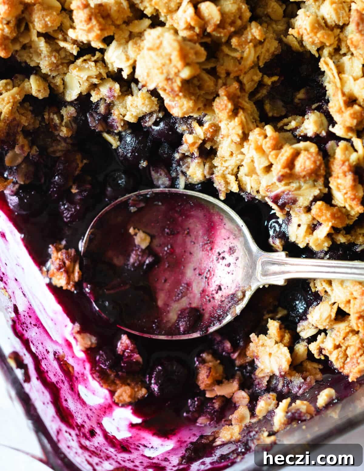 a close up of a blueberry crisp with a spoon in it.