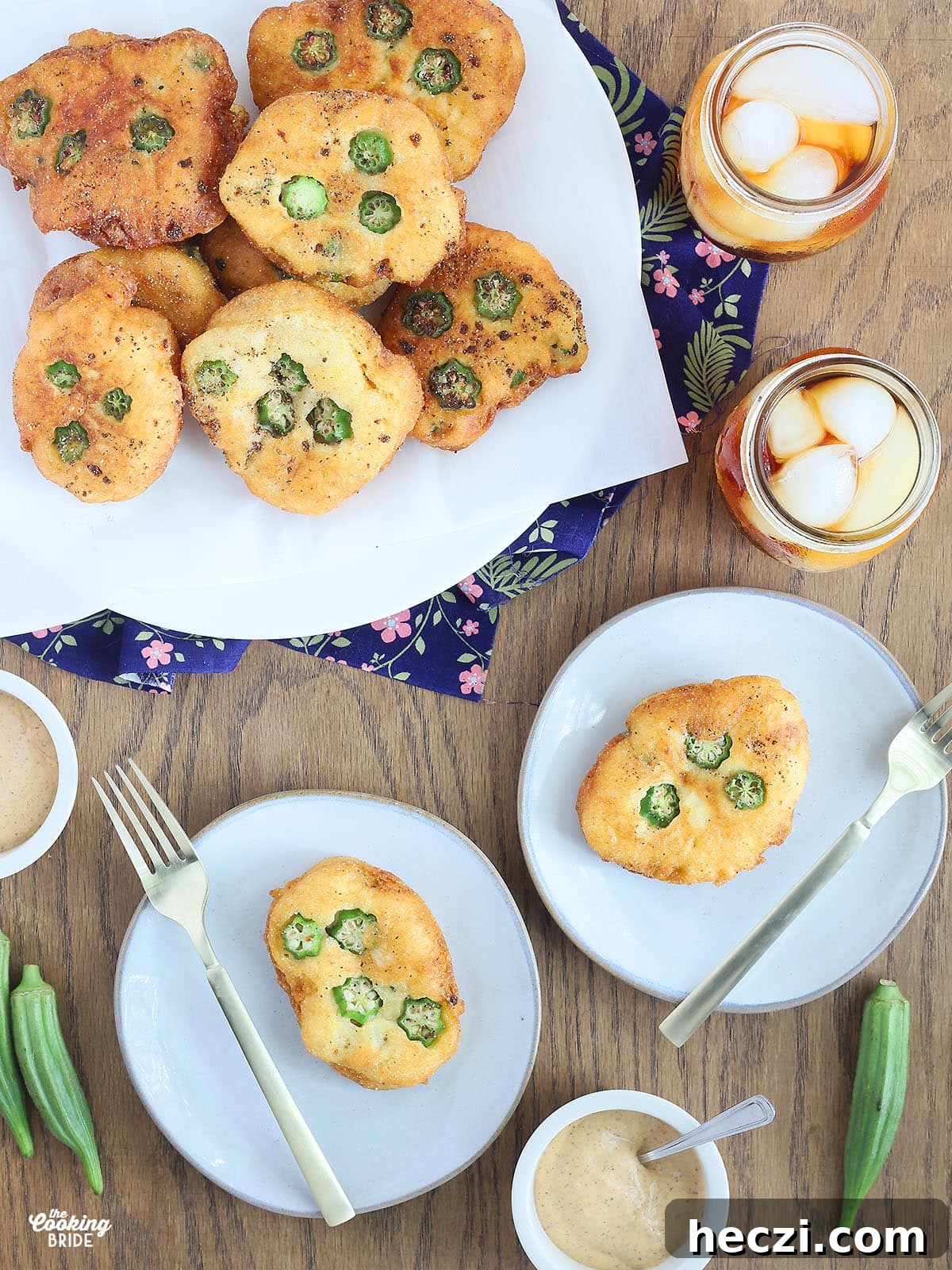two okra hoe cakes on white plates with gold forks to the side. A large platter of hoe cakes and glasses of iced tea are to the side.