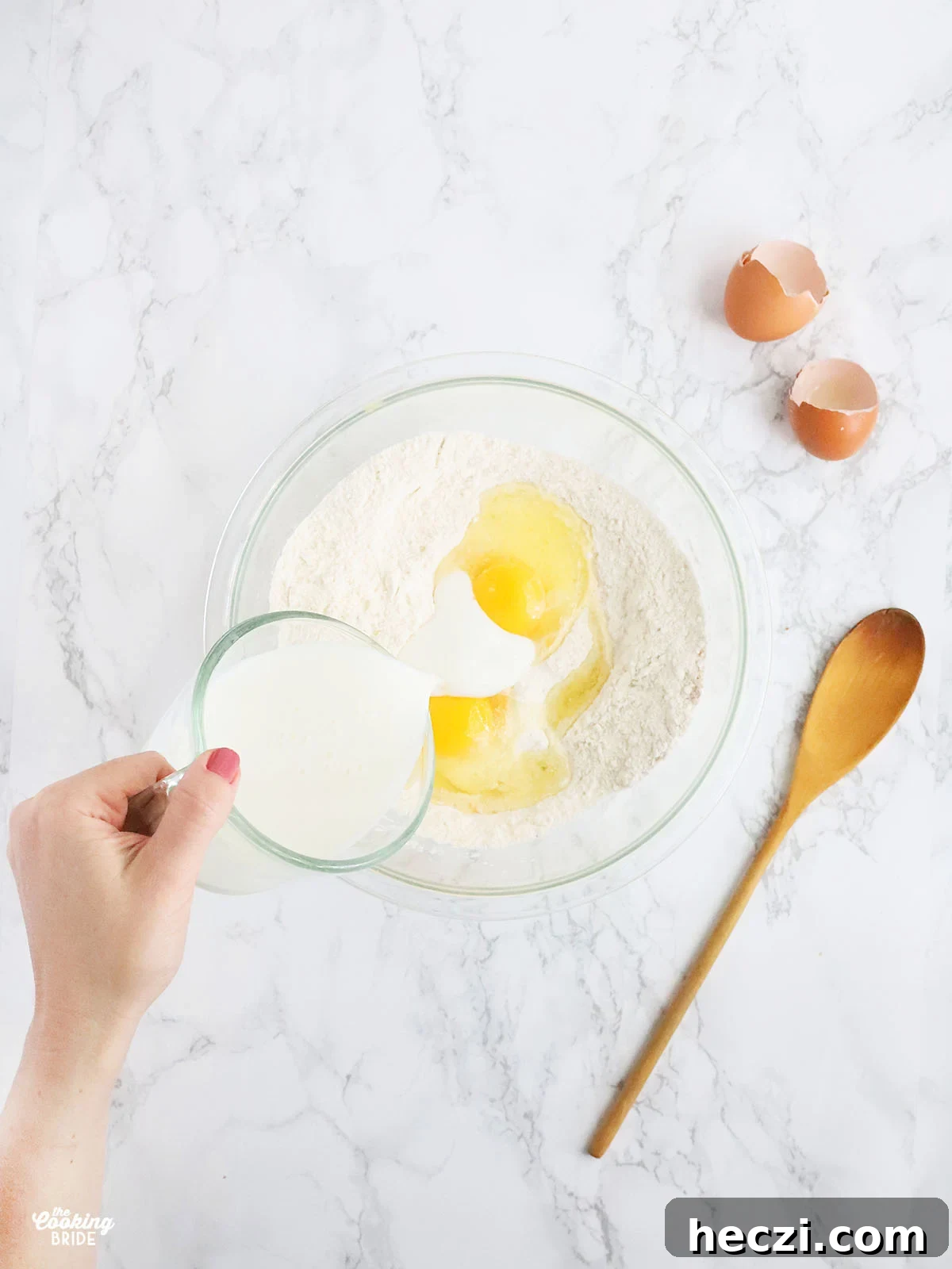 hand pouring milk into a mixing bowl with cornmeal and eggs.