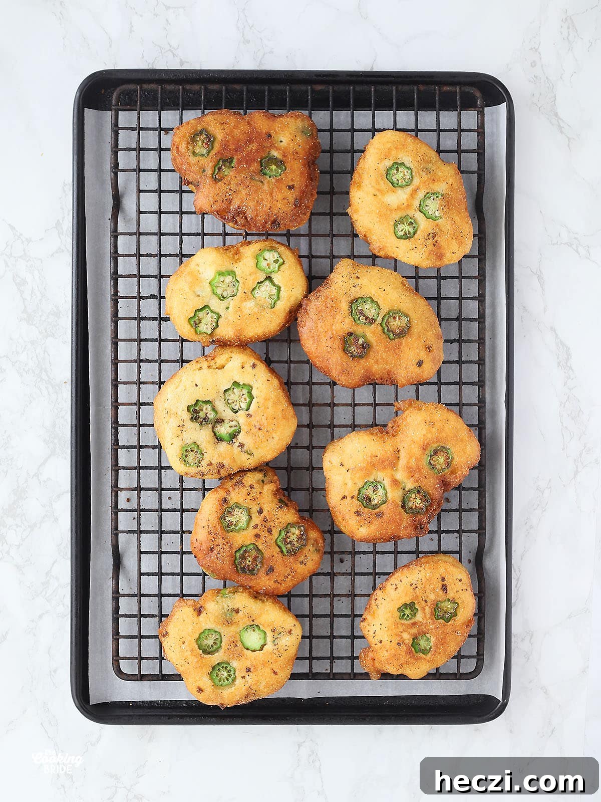 Fried okra hoe cakes draining on a rack over parchment paper.