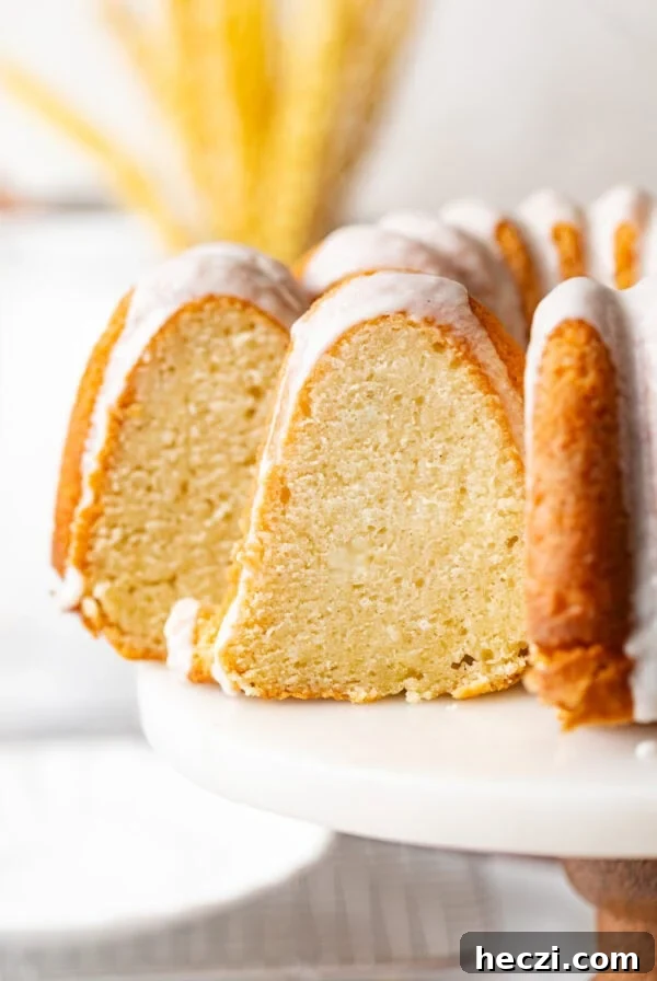 sliced sour cream pound cake on a cake stand topped with vanilla glaze.