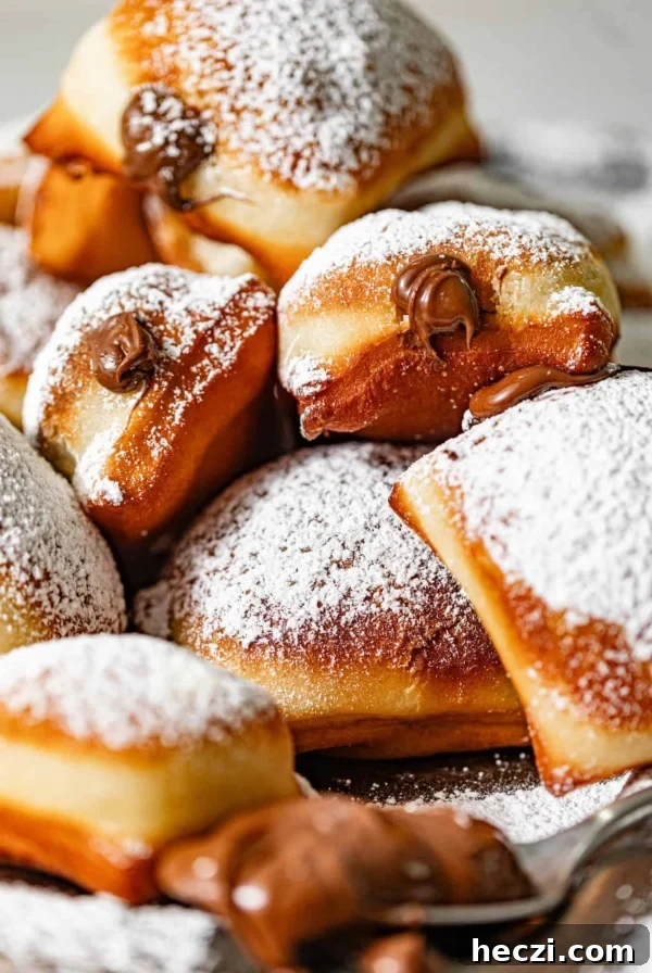 nutella beignets stacked on top of each other and covered in powdered sugar with nutella oozing from the center.