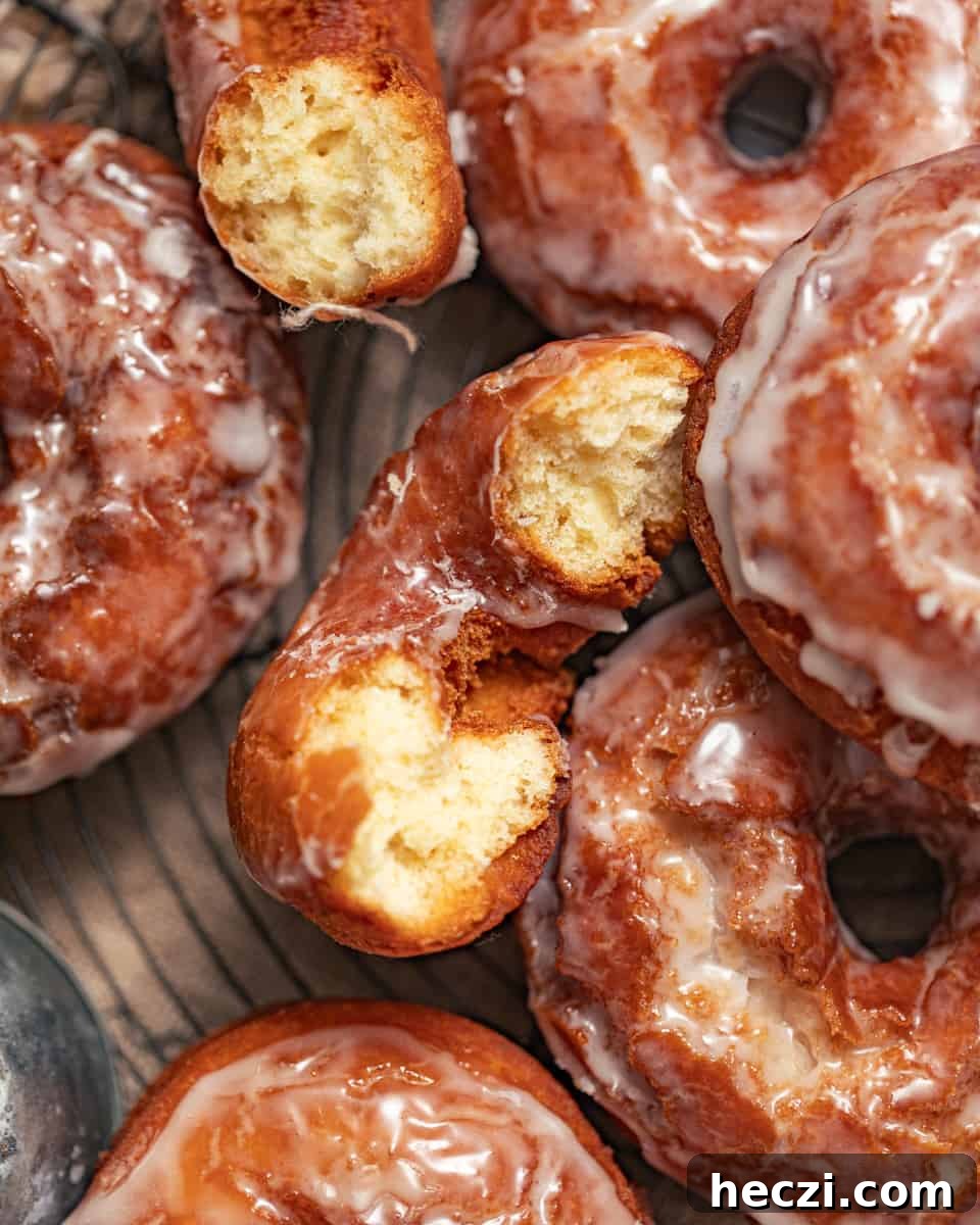 sour cream donuts on a wire rack with one donut cut in half to see the inside of the donut.
