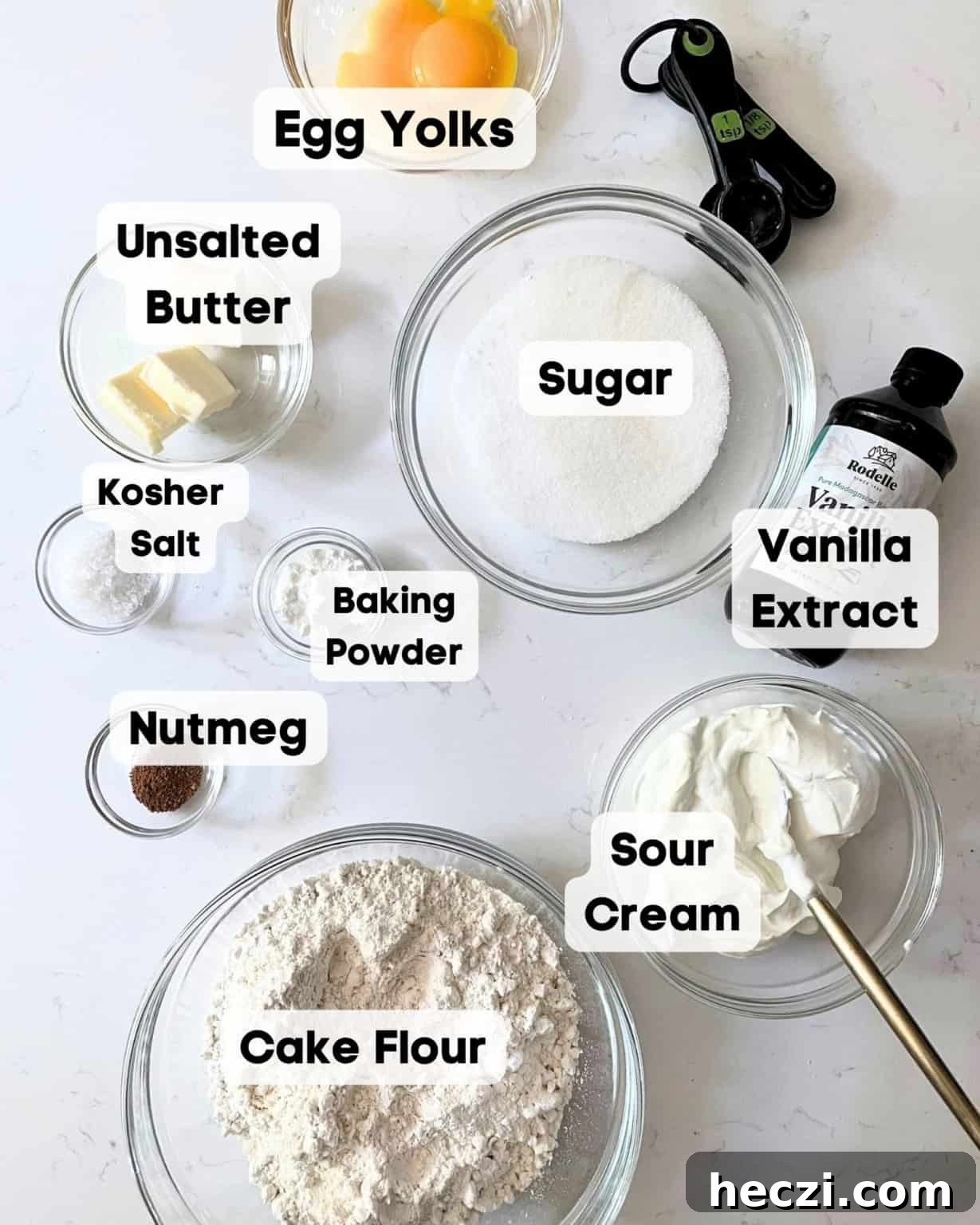 ingredients to make old fashioned donuts on a white surface - cake flour, sugar, baking powder, egg yolks, butter, nutmeg, salt, vanilla extract, and sour cream.