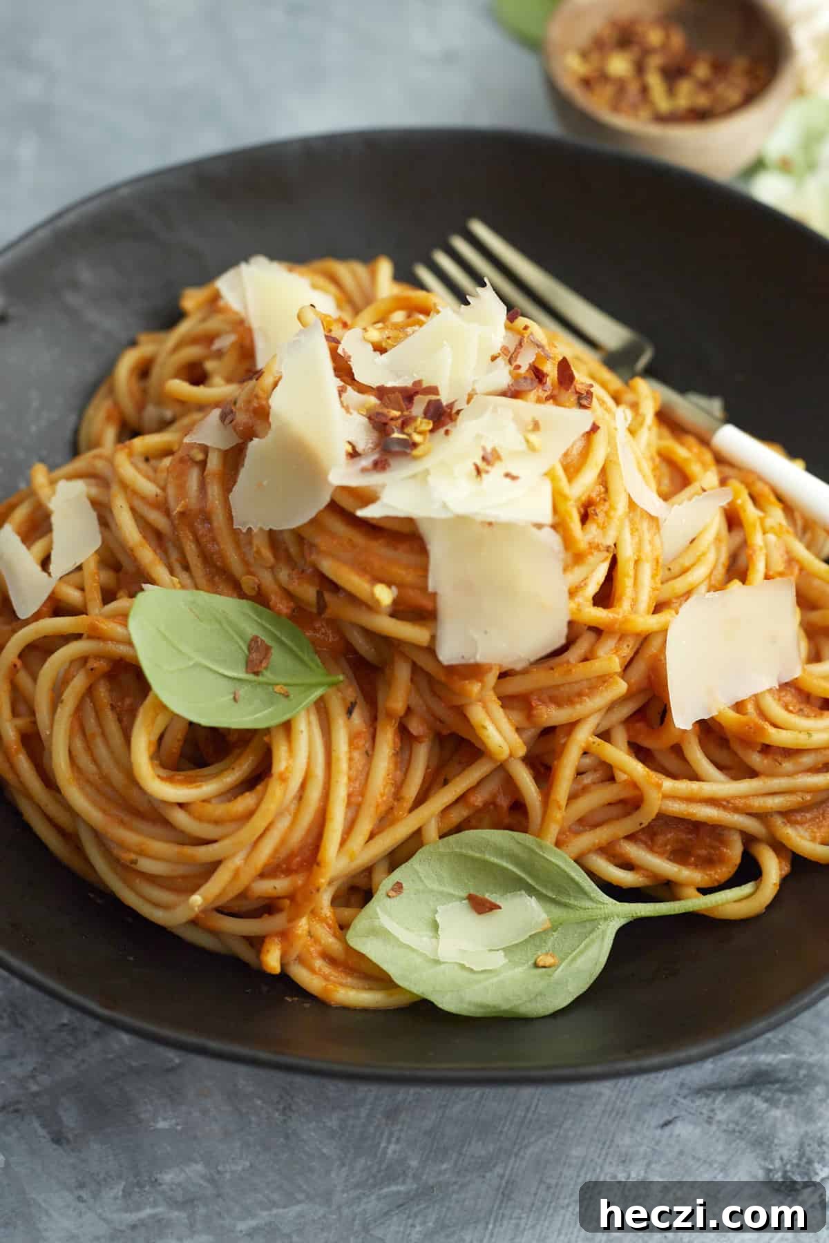 Spicy Baked Spaghetti Arrabbiata with Crispy Cheese Topping 5 a black plate with a pile of arrabiata sauce spaghetti bake topped with Parmesan cheese, basil leaves, and red pepper flakes