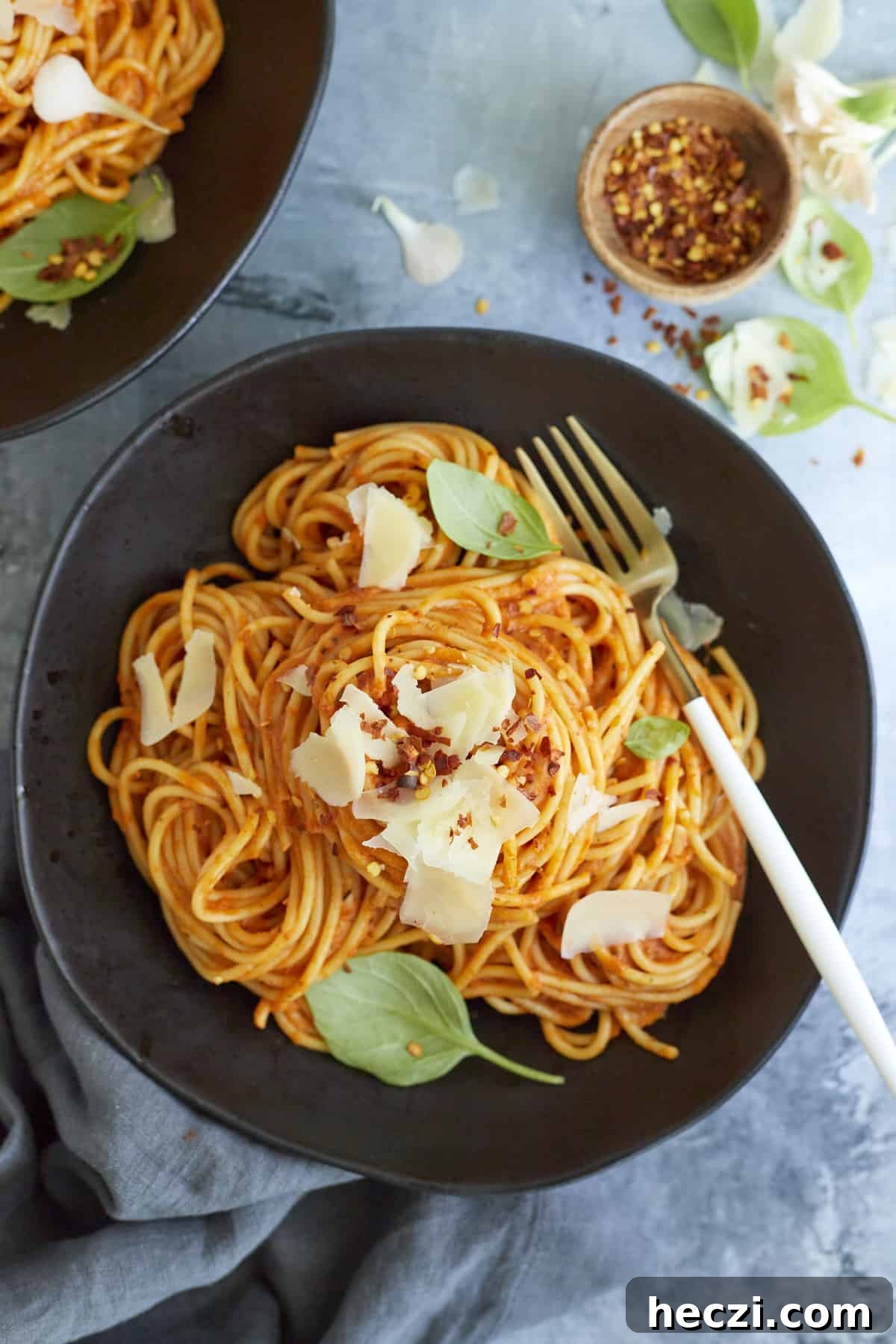 Spicy Baked Spaghetti Arrabbiata with Crispy Cheese Topping 6 A serving of arrabiata sauce spaghetti on a black plate topped with fresh Parmesan cheese, basil leaves, and red pepper flakes with a fork on the side.