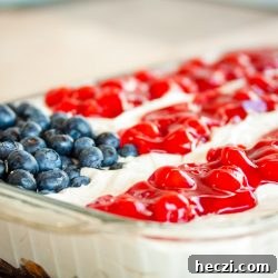 Fluffy white whipped cream mix over crumbled angel food cake topped with blueberries and cherry pie filling in the design of an American flag in a 9x12 glass pan