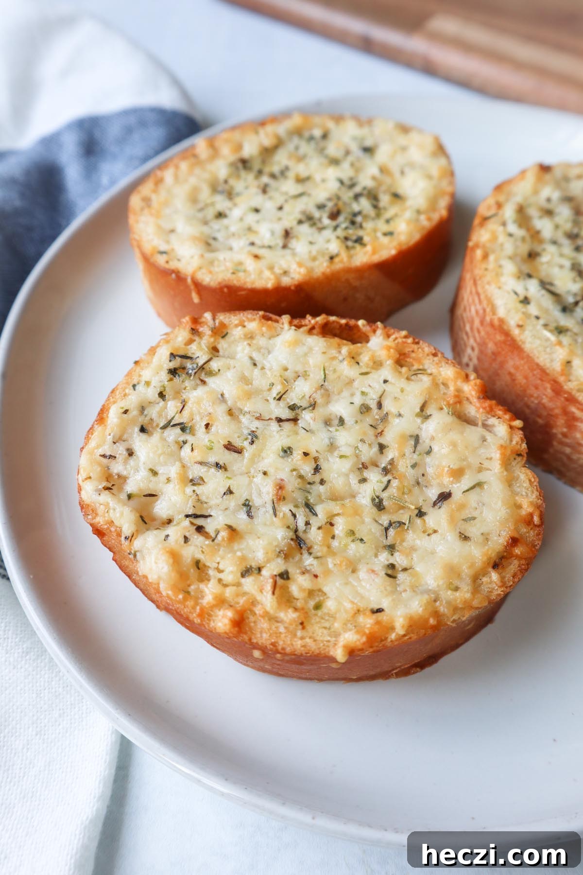 white plate with three slices of french bread topped with cheese, butter, and italian seasoning
