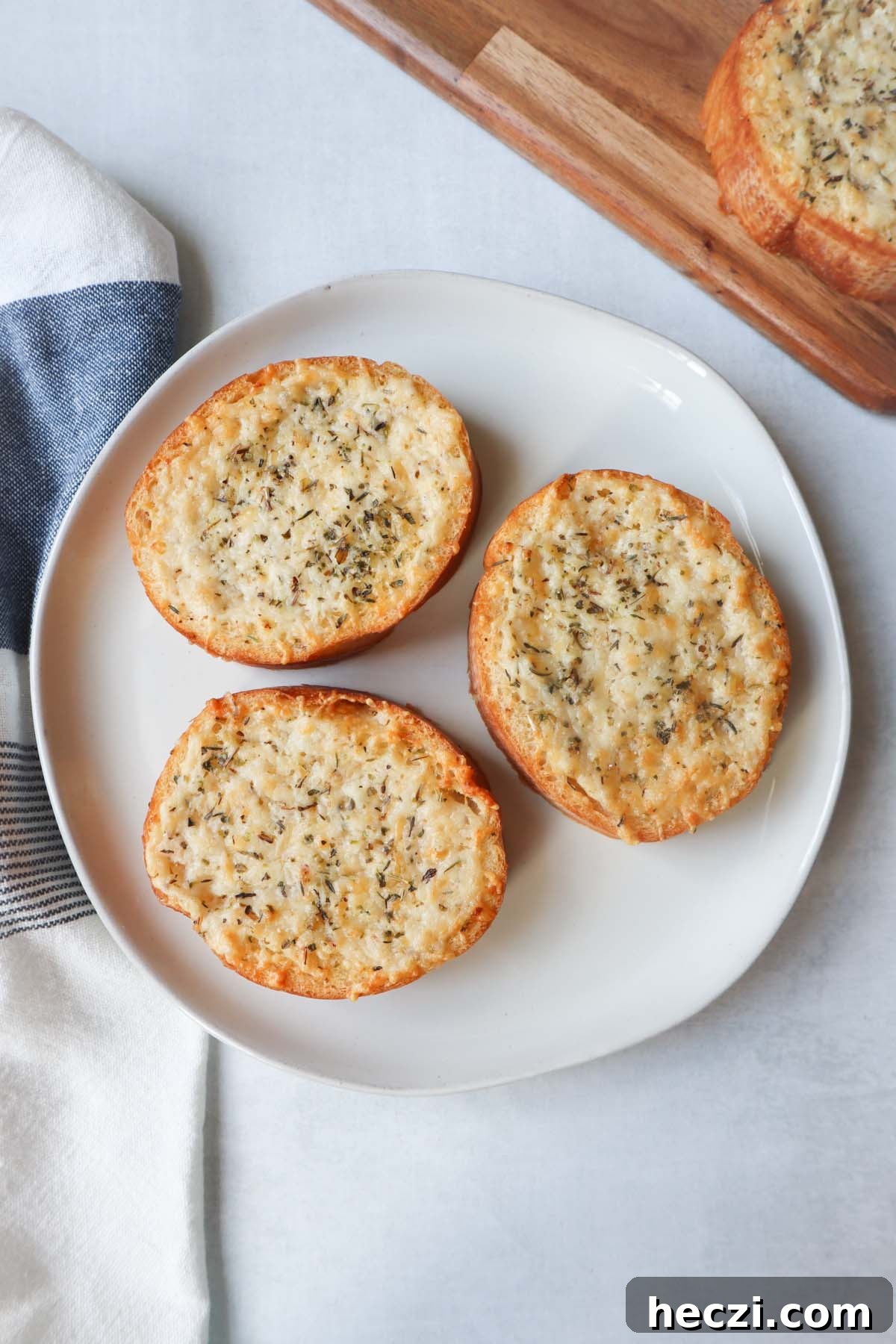 white plate with three slices of french bread topped with cheese, butter, and italian seasoning