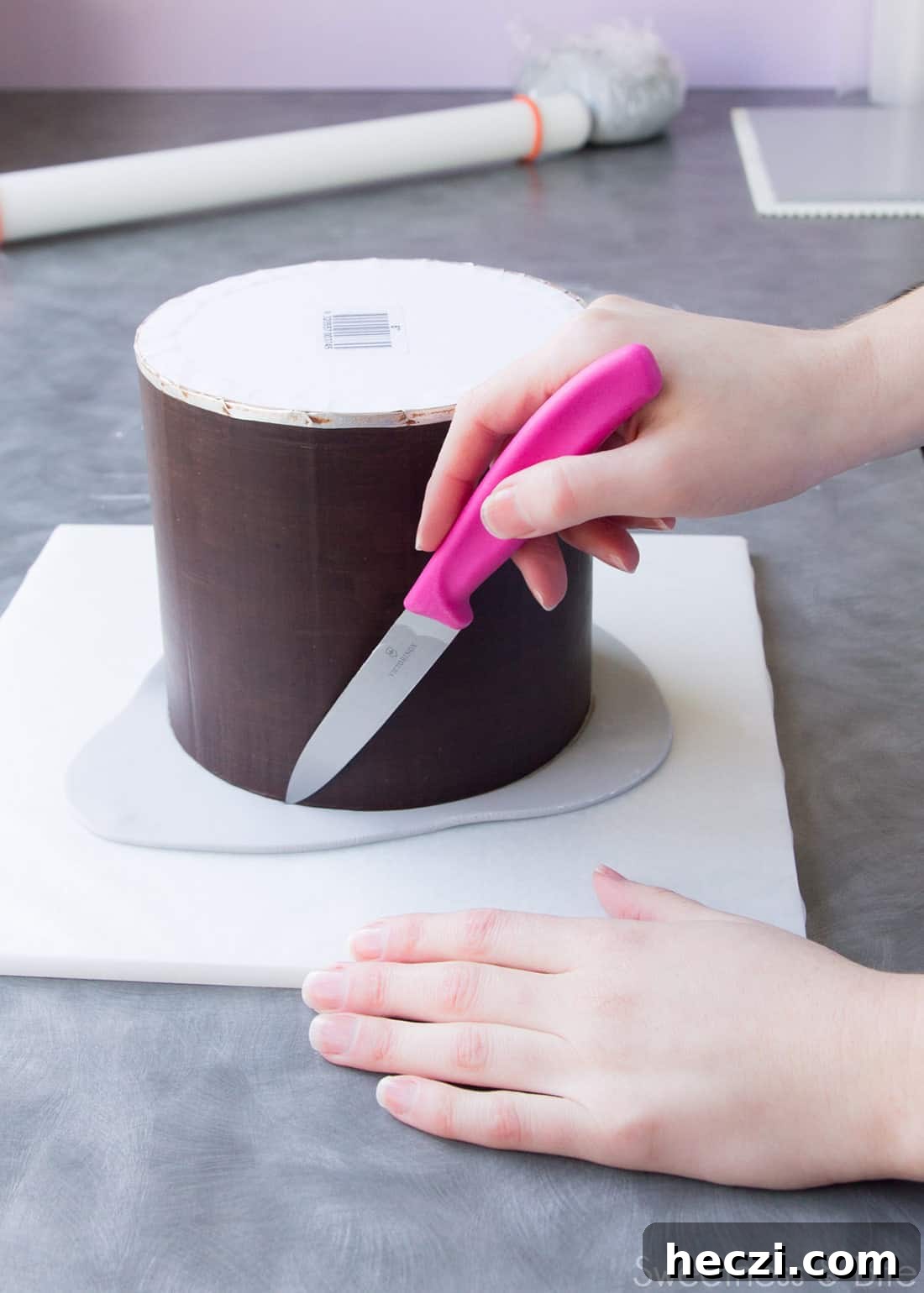 A hand using a small knife to trim the fondant on the upside down cake.