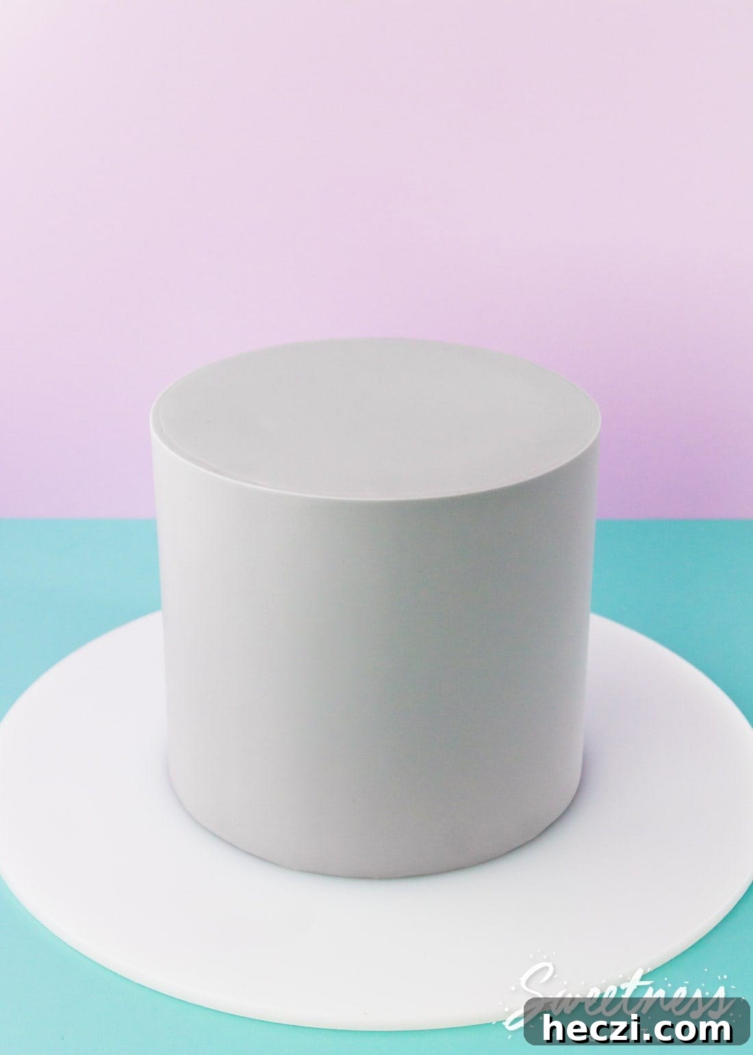 A cake wrapped in pale grey fondant on a purple and teal background.