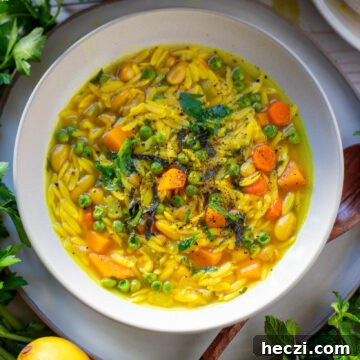 white bowl with Lemon Orzo Soup with fresh herbs and lemons.