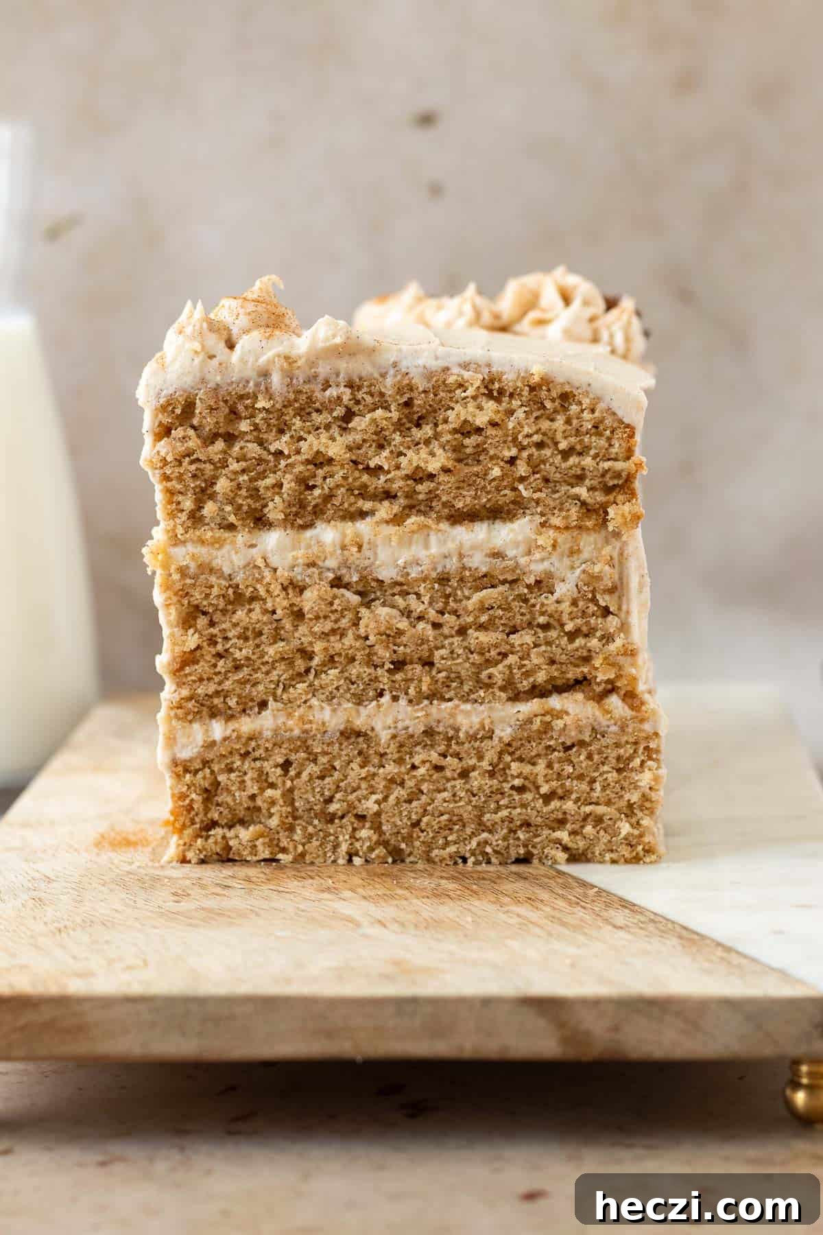 chai cake sliced open showing 3 layers of cake and 2 layers of frosting, sitting on a wood cutting board