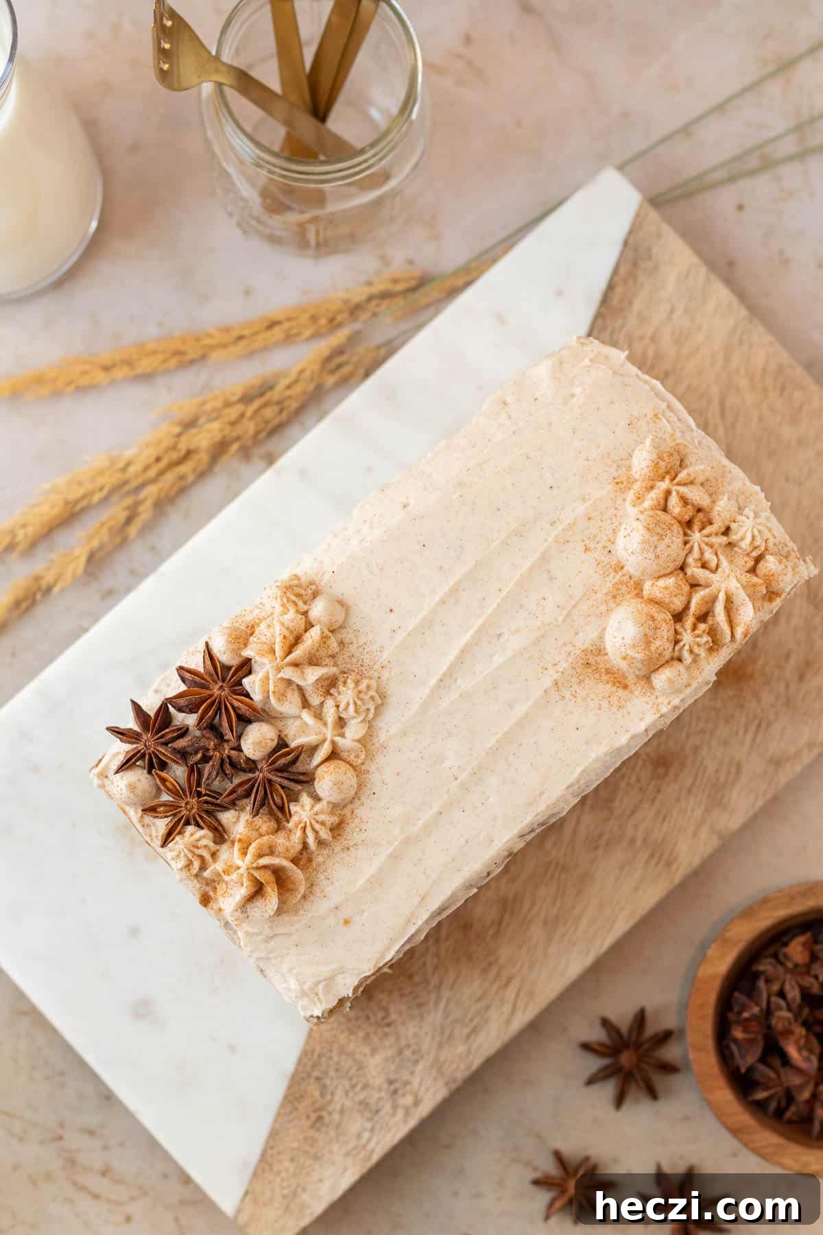 a rectangular chai cake decorated with rosettes of frosting and star anise pods sitting on a wood and marble cutting board
