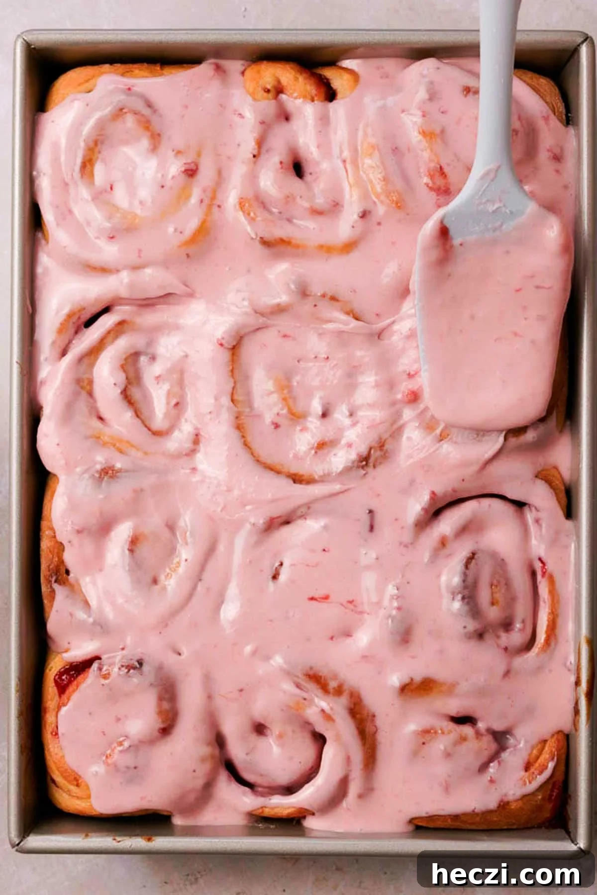 Strawberry Cinnamon Rolls with Cream Cheese Glaze 20 spreading pink glaze over baked strawberry cinnamon rolls