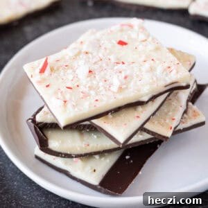 Homemade Peppermint Bark Recipe: Quick Holiday Chocolate Candy 16 Peppermint bark stacked on a white plate with more peppermint bark in the background.