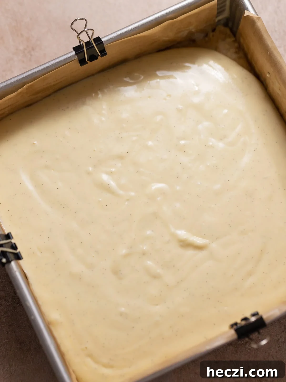 Vanilla cheesecake batter poured over the shortbread crust in a baking pan.