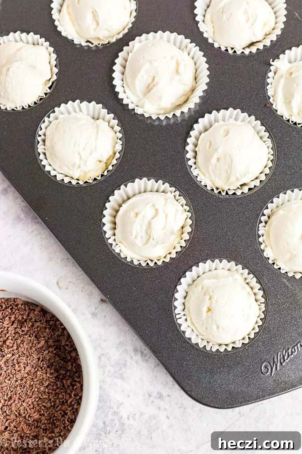 Keto Cheesecake Fat Bomb Recipe for Low-Carb Snacks 4 Keto Cheesecake Fat bombs in a cupcake holder in a muffin pan with a bowl of shaved chocolate.