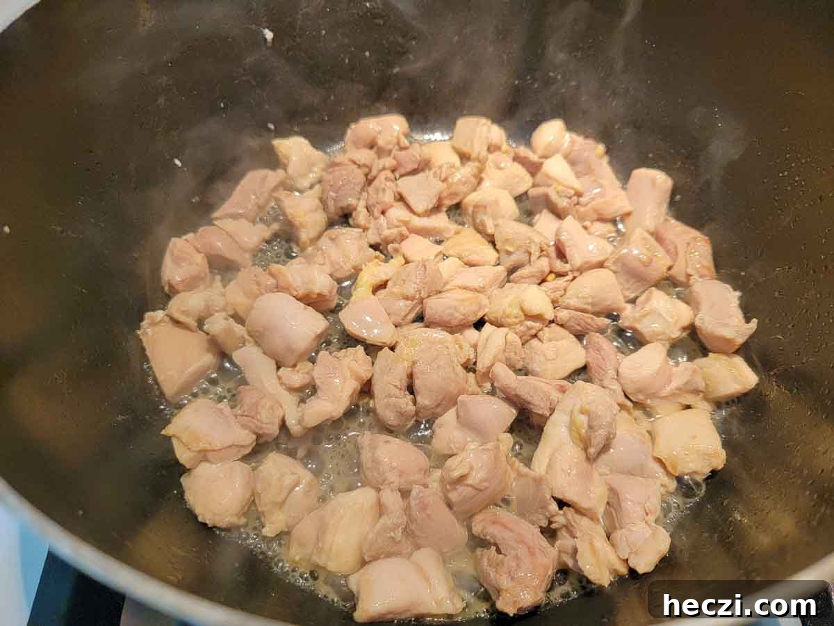 cubed chicken thighs cooking in a pan.