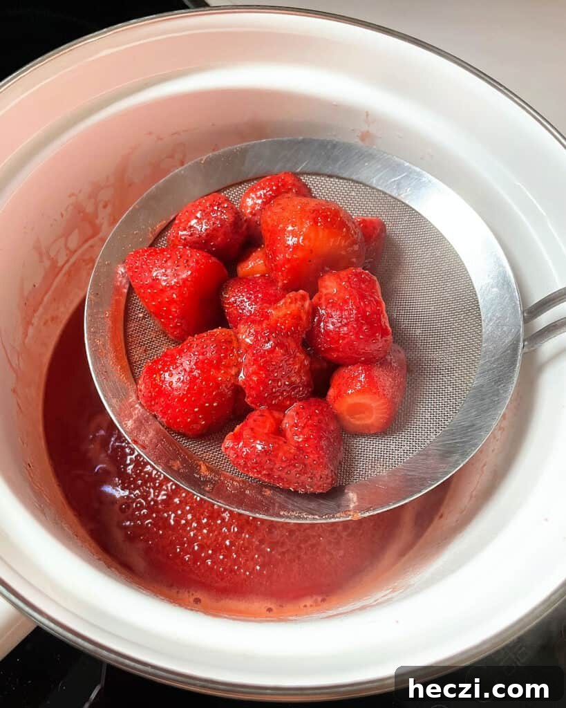 4-Ingredient Strawberry Compote Recipe for Fresh Homemade Jam 6 Skimming whole cooked strawberries from a white saucepan.