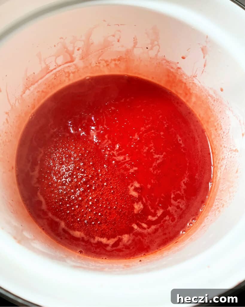 4-Ingredient Strawberry Compote Recipe for Fresh Homemade Jam 7 White saucepan with simmering strawberry juice.