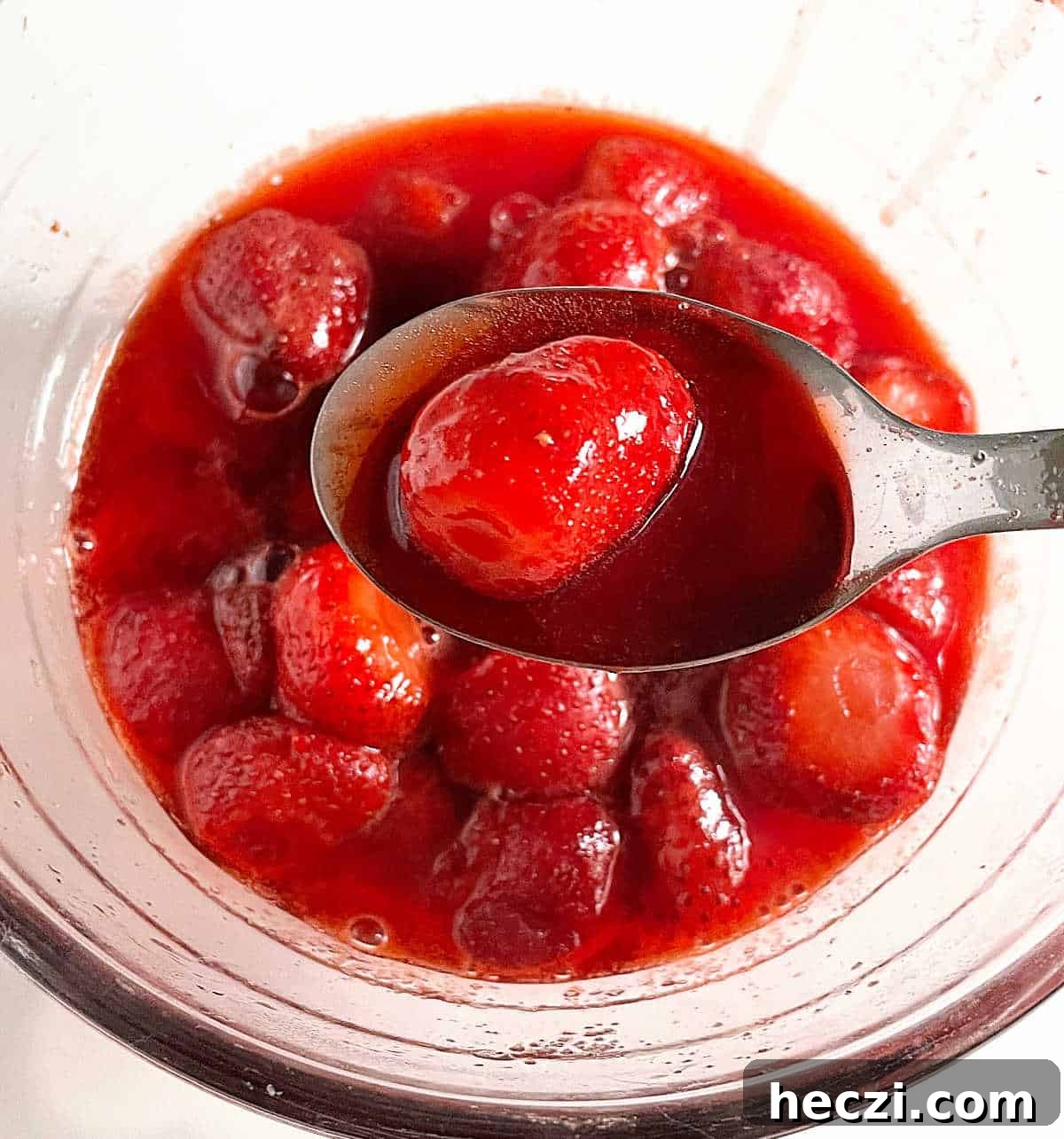 4-Ingredient Strawberry Compote Recipe for Fresh Homemade Jam 8 Strawberry compote on spoon with bowl containing more compote below, white background.